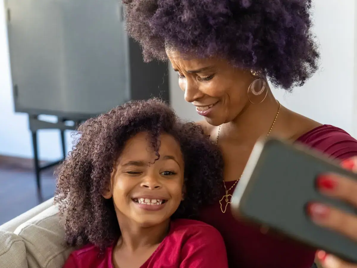 A mother and her daughter smiling at a phone together